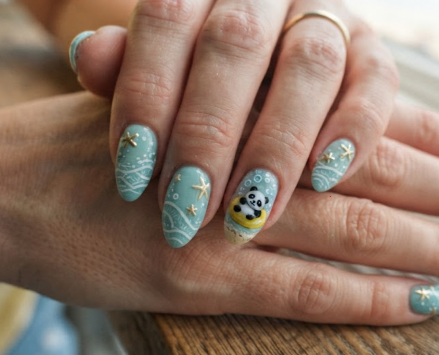 In this image, medium-length almond-shaped nails with a relaxing seafoam blue base are shown. The accent nail shows a panda lounging on a tiny yellow beach floatie in the water. Others feature gentle ocean waves, white sea foam lines, and tiny starfish accents. The hand wears a light yellow t-shirt.
