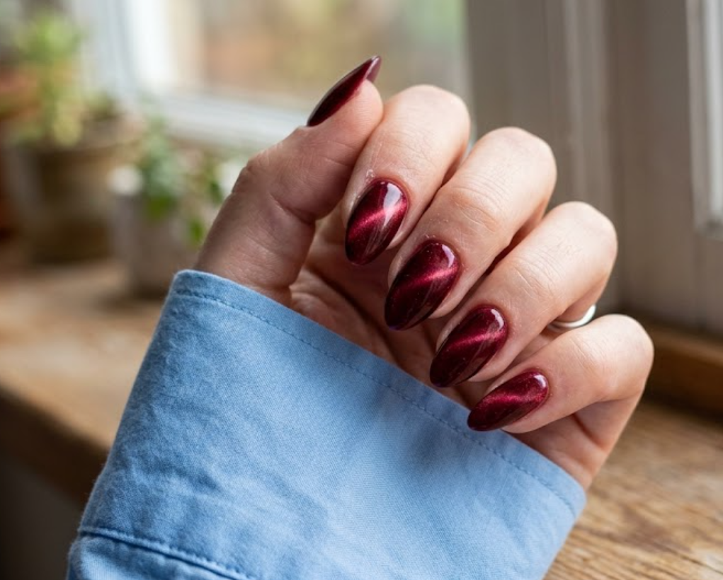 imagIn this close-up photo, Chinese New Year nails featuring almond deep red magnetic velvet cat-eye tips with diagonal light shifts are shown on a real hand wearing a sky blue shirt.e