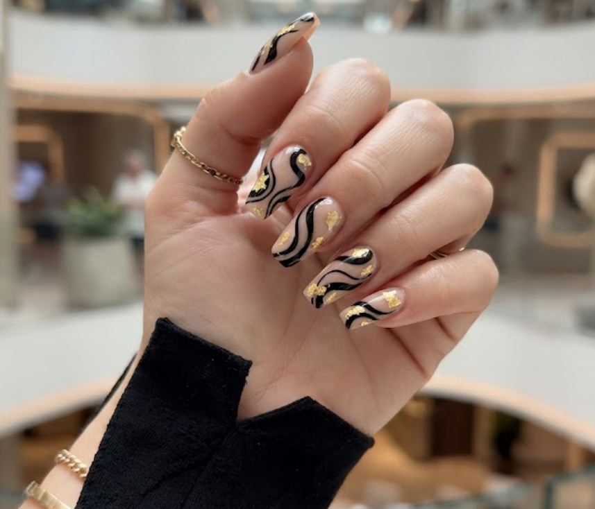Coffin-shaped honeymoon nails featuring black and nude abstract swirls with gold foil details.