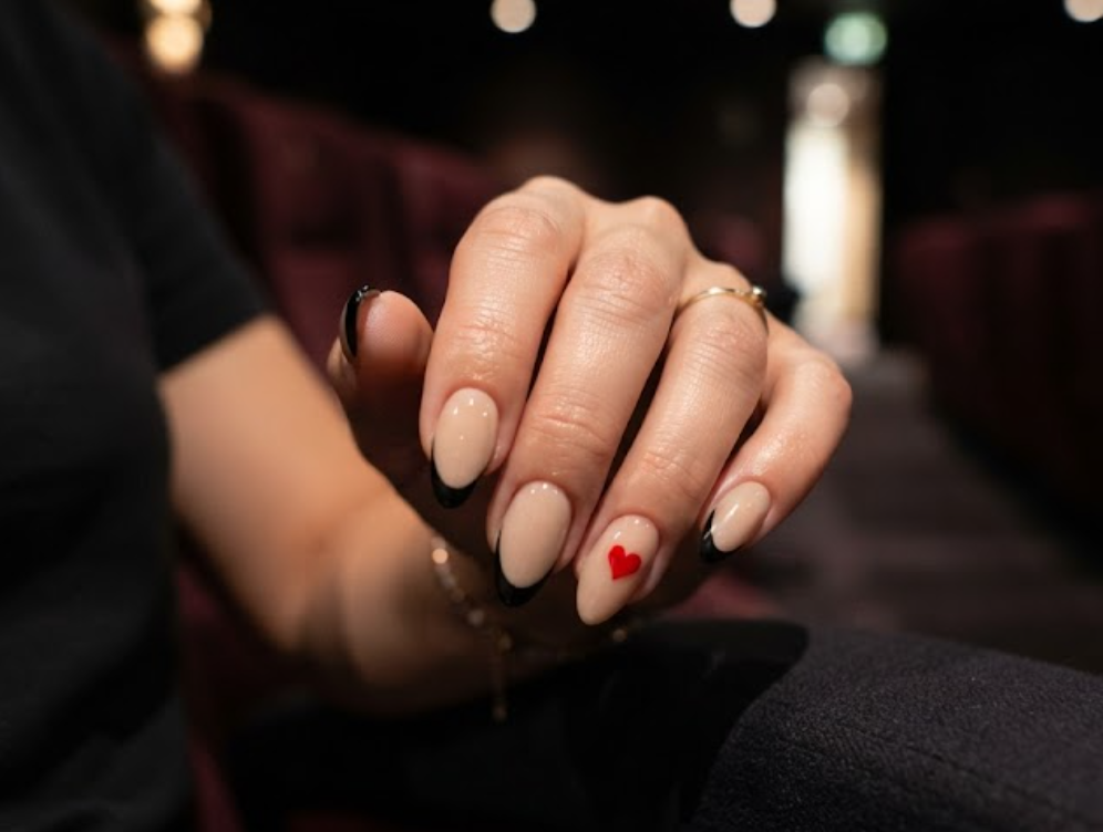 Almond-shaped honeymoon nails with matte black French tips and a small red heart accent.