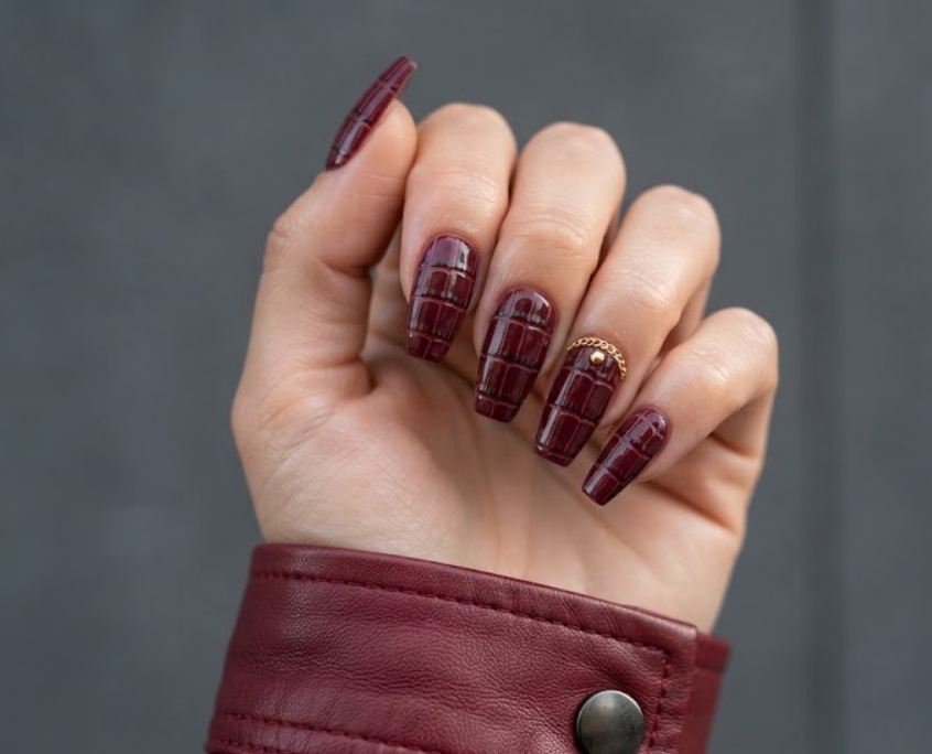 Coffin-shaped burgundy crocodile print honeymoon nails with metallic gold chain details along the cuticle.