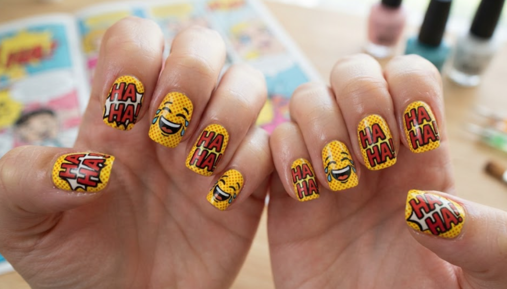 In this image, yellow comic nails feature HA HA lettering, laughing cartoon faces and halftone dots.