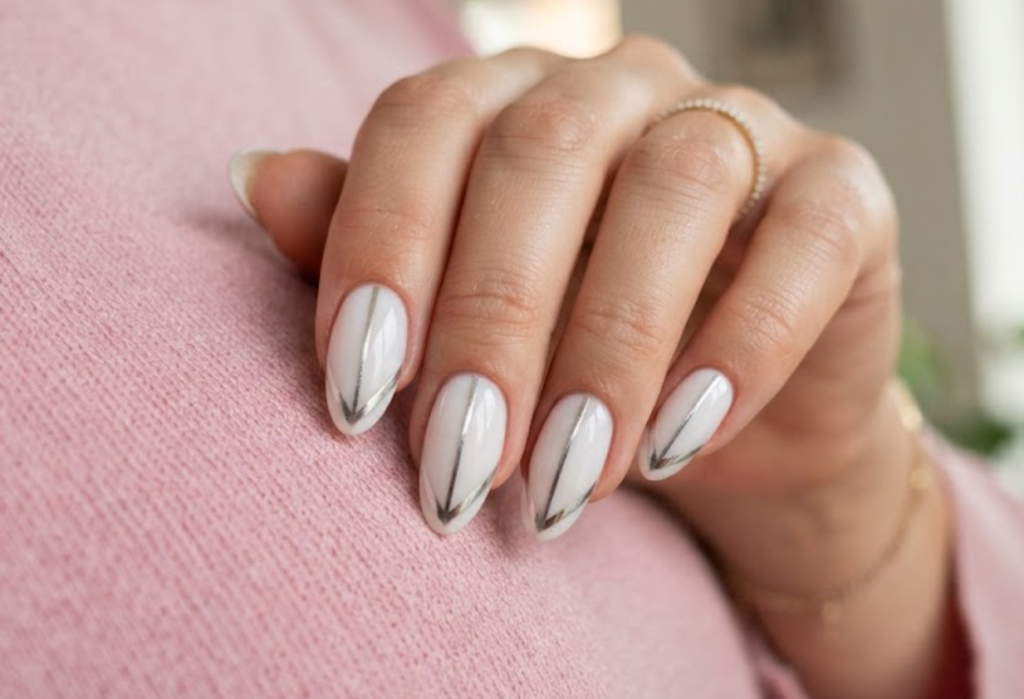 In this image, a woman's full hand displays milky white nails with silver chevron tips and a vertical hairline, wearing a pink shirt.