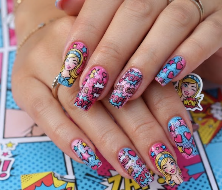 In this image, pink and blue comic nails feature a cartoon girl, hearts, stars and WOW speech bubbles.