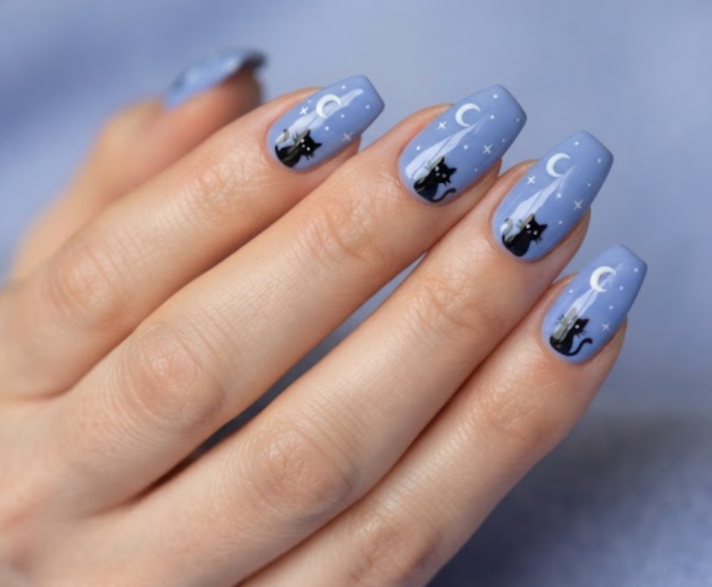 In this image, periwinkle blue nails with cartoon cats and crescent moons