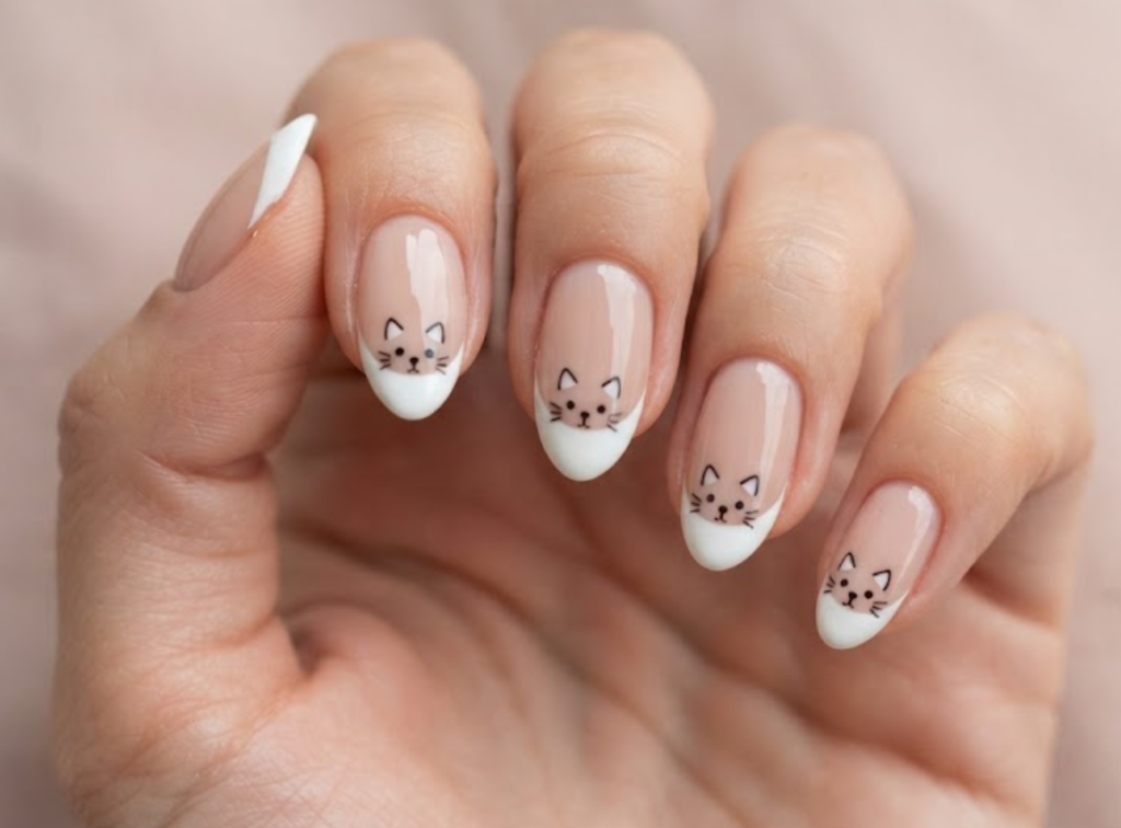 In this image, blush nude French tip nails with tiny cartoon cat faces