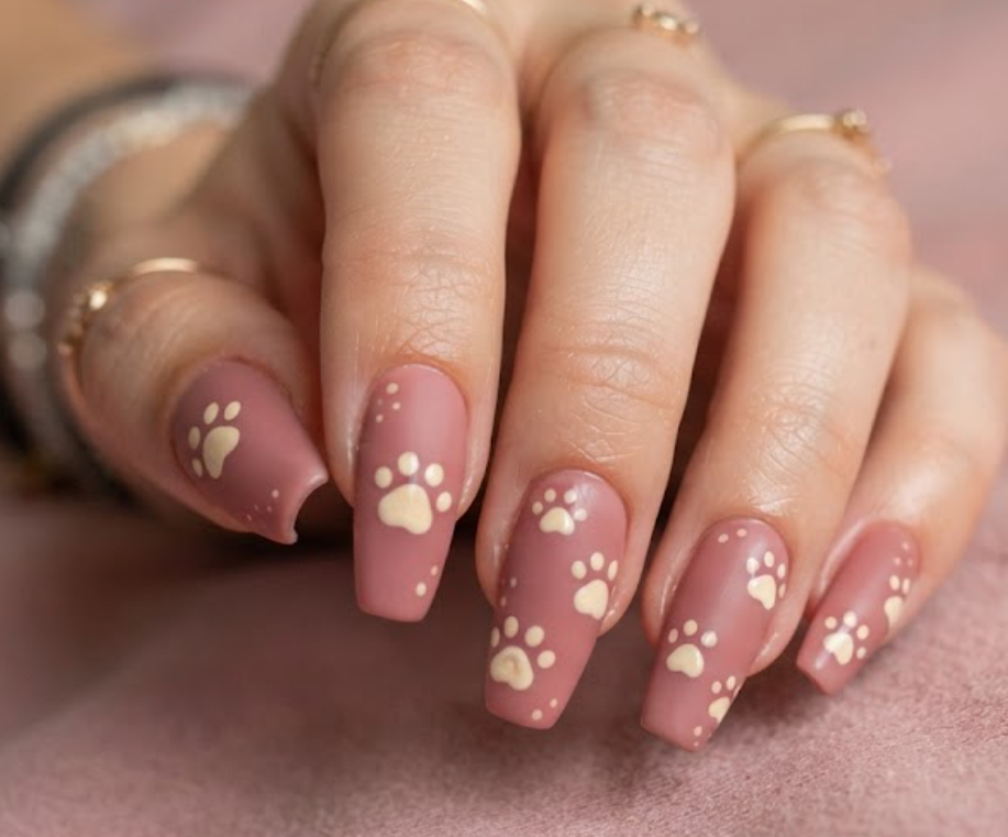 In this image, dusty rose nails with cartoon kittens and cream paw prints