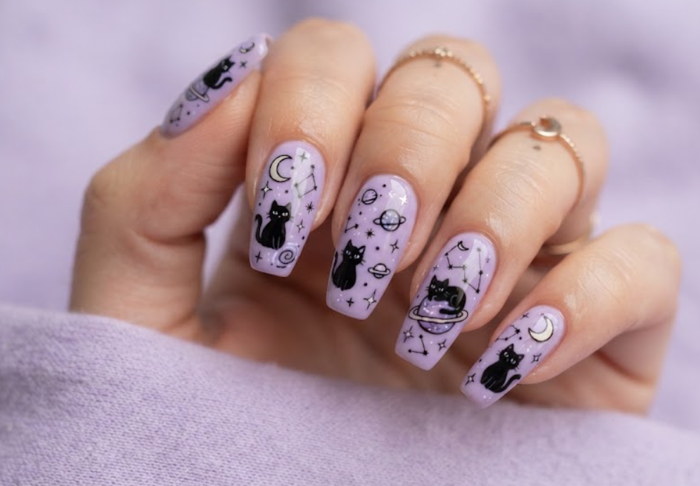 In this image, lavender galaxy nails with black cartoon cats and stars