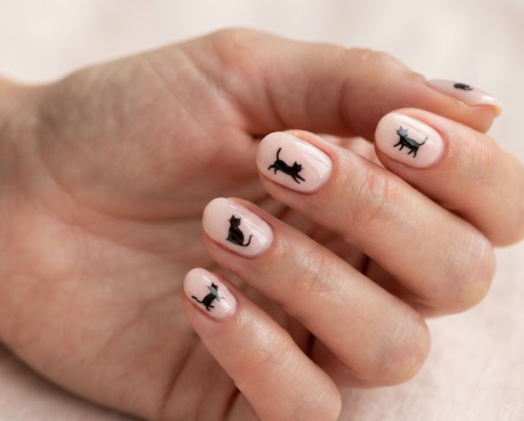 In this image, cream pink nails with playful black cartoon cat silhouettes