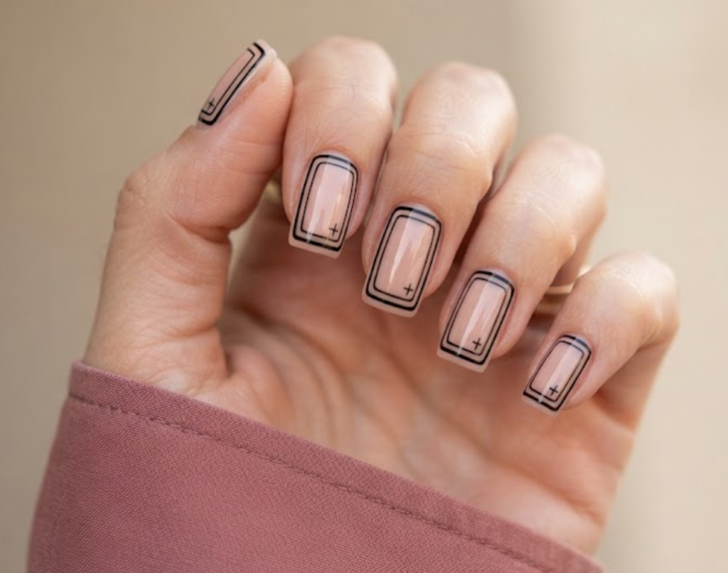 In this image, a woman's full hand highlights nude pink nails with double rectangular frames and cross stamps, wearing a rose shirt.