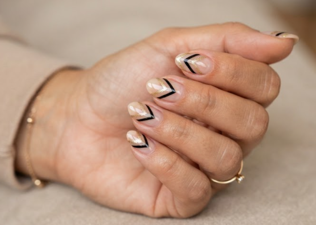In this image, a woman's full hand features transparent nude nails with inverted chevron stacks and bare halves, wearing a beige shirt.