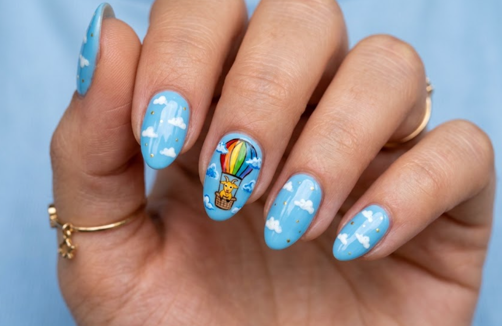 In this image, baby blue nails with a cartoon goat riding a hot-air balloon
