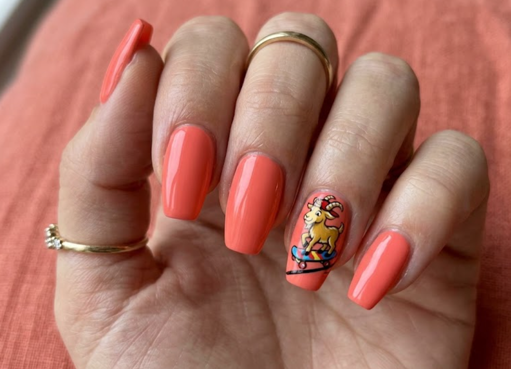 In this image, coral nails with a cartoon goat riding a skateboard