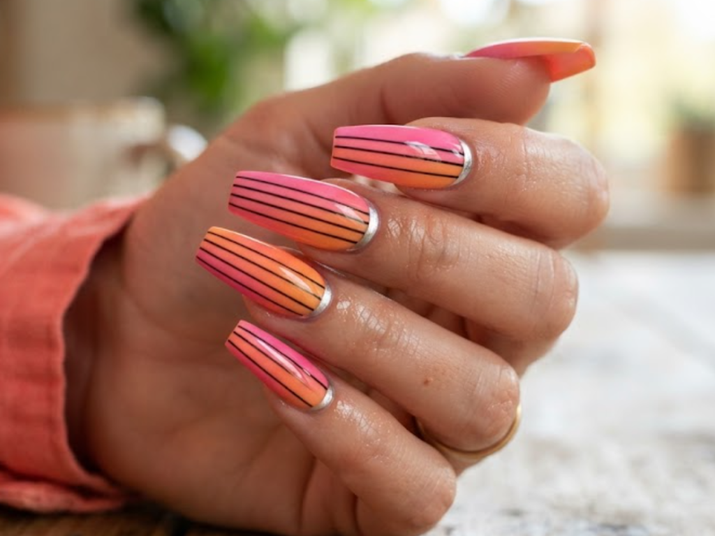 In this image, a woman's full hand shows pink-orange ombre nails with black horizon lines and a silver arc, wearing a coral shirt.