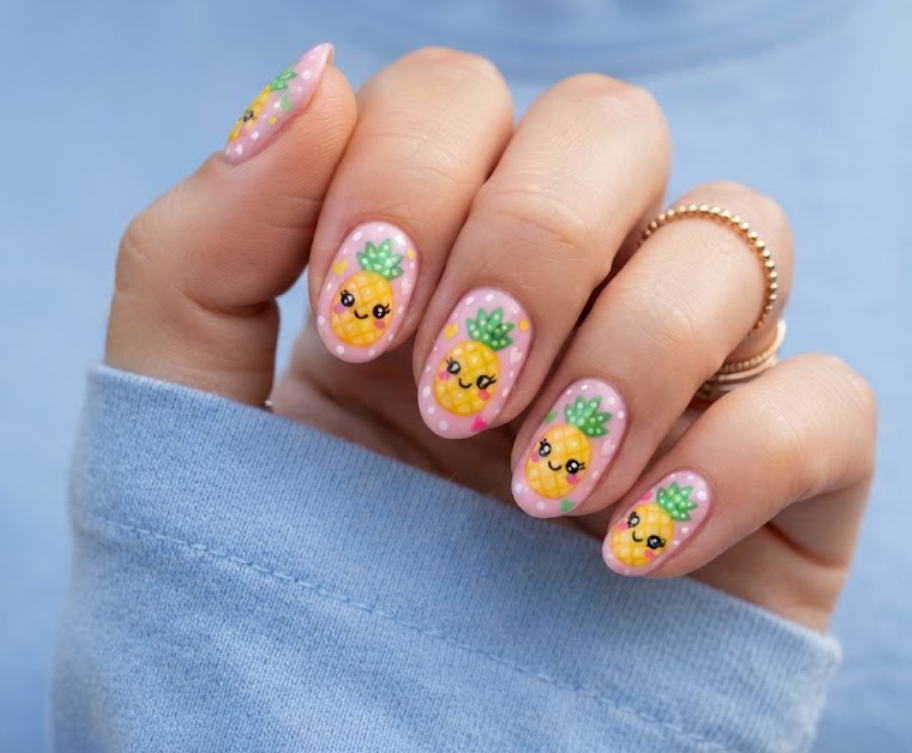 in this image, a hand in a blue shirt features kawaii anime pineapple nails with cute smiling faces.