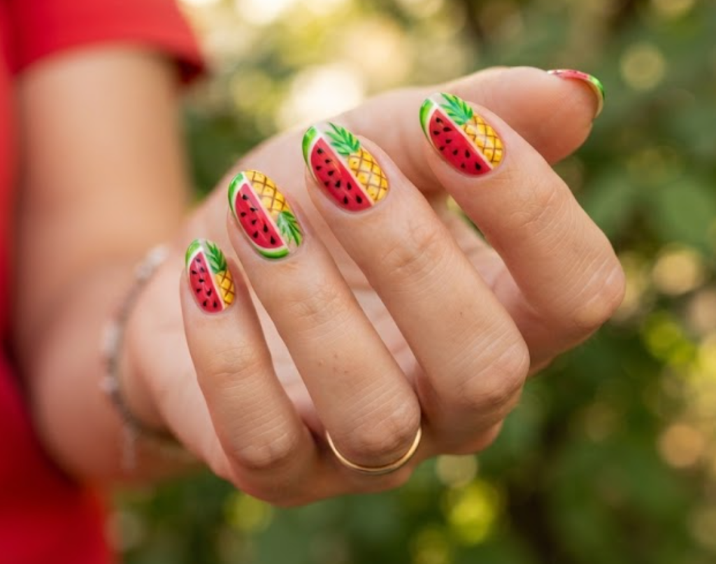 in this image, a hand in a red shirt features fun watermelon and pineapple split-nail art.