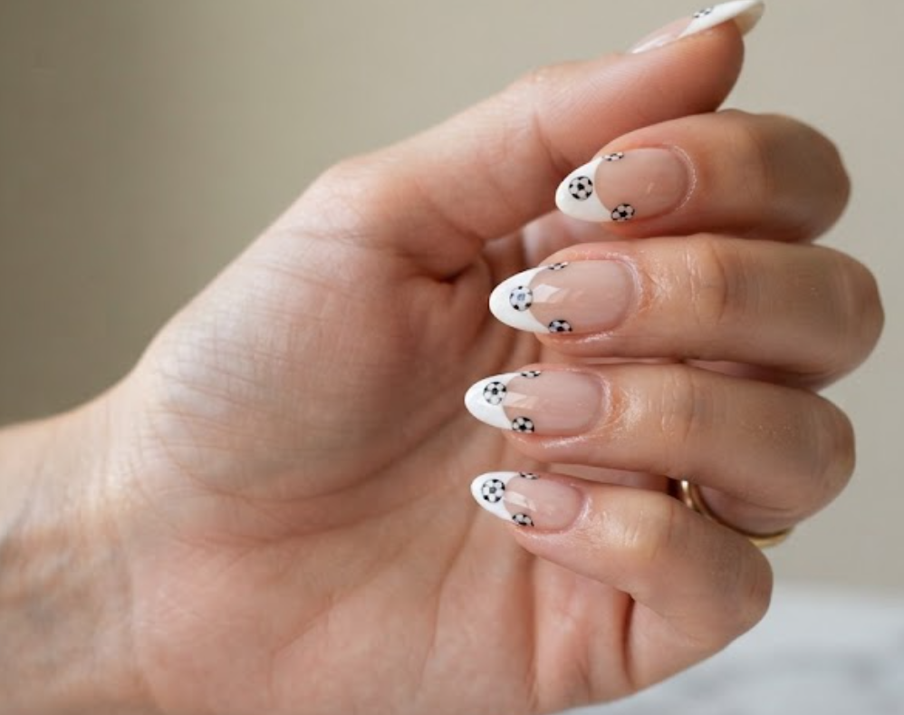 In this image, black and white soccer ball French tip nails on an almond-shaped manicure.