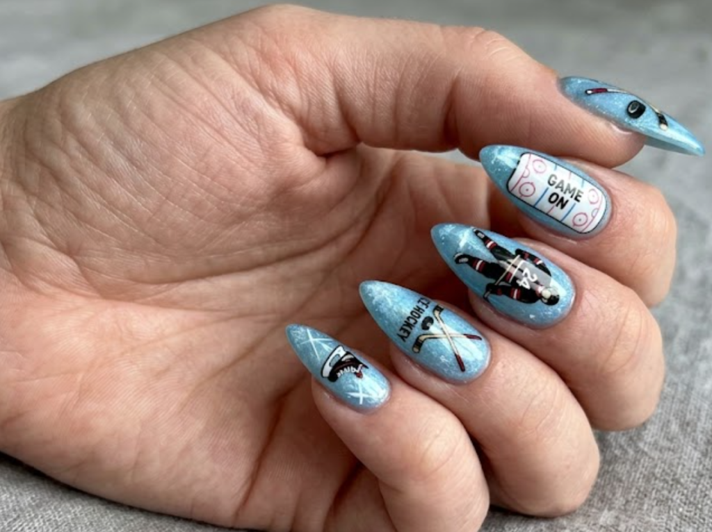 In this image, hockey nails with black hockey pucks, hockey sticks, ice rink lines, and blue accents.age