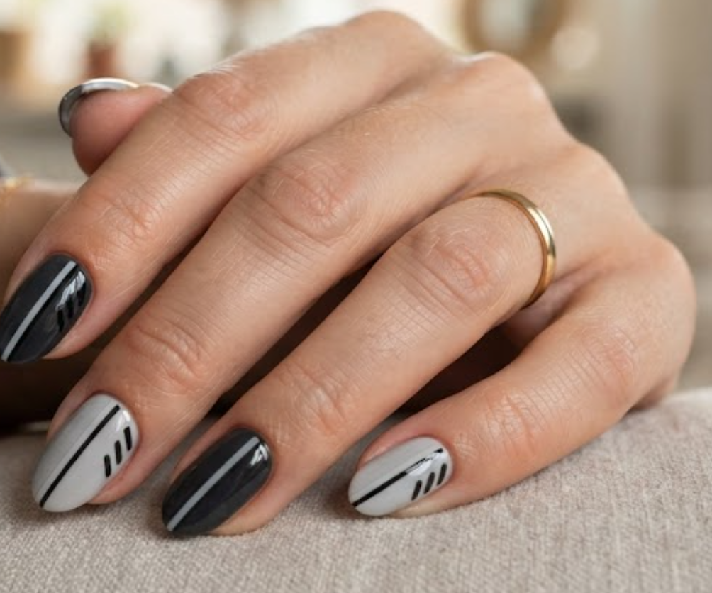 In this image, a woman's full hand features grey and charcoal nails with parallel vertical lines and diagonal dashes, wearing a steel shirt.