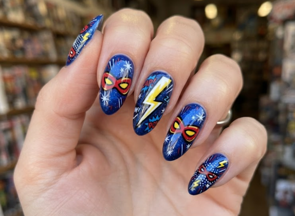 In this image, blue comic nails feature a superhero mask, lightning bolts and black action lines.