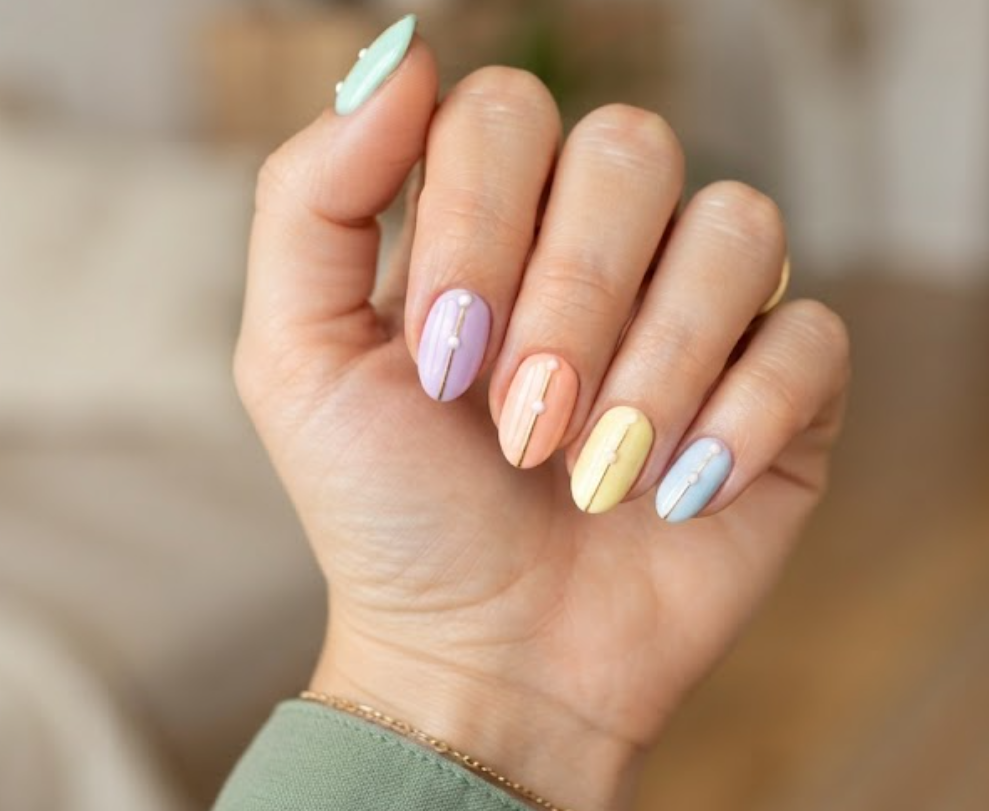 In this image, a woman's full hand showcases pastel nails with gold vertical lines and white dots, wearing a sage green shirt.